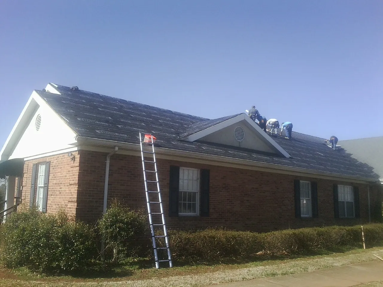 Crew tearing shingles off a brick ranch roof with a ladder set — Emergency Roof Repair work by our crew in Addison