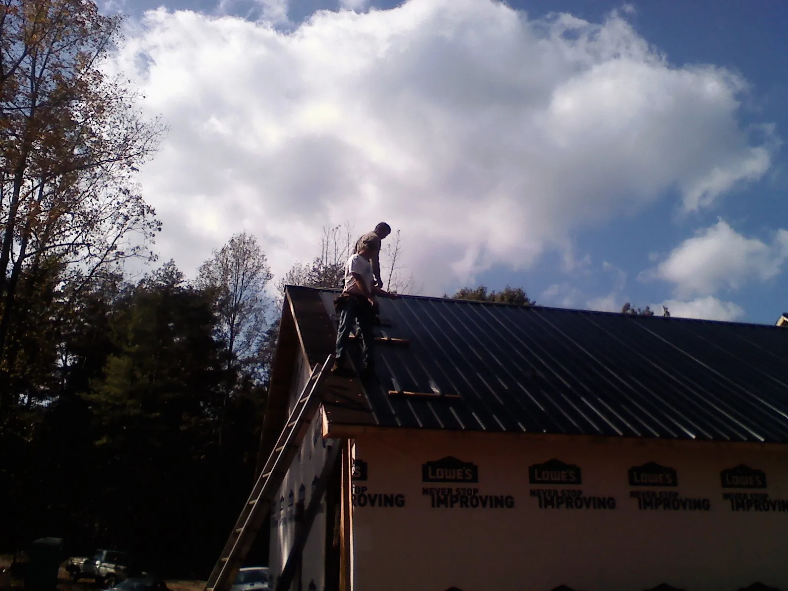 Roofer fastening dark metal panels high against a cloudy sky, from a Roof Inspection job in Addison